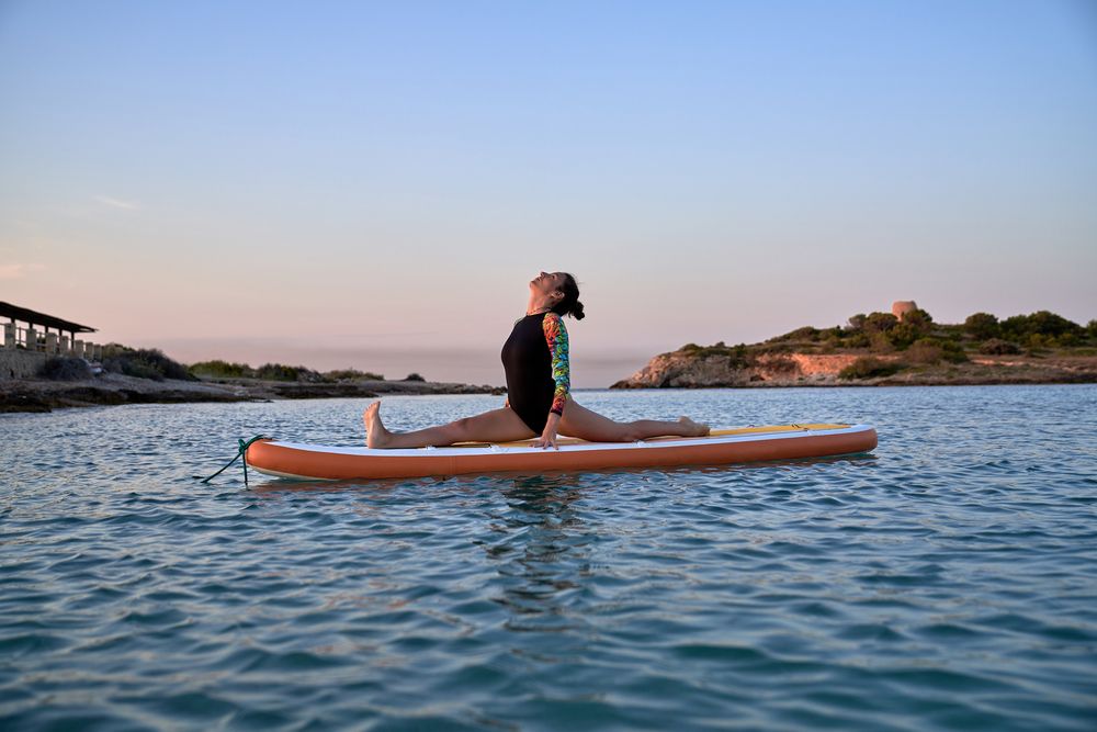 Sporty female athlete taking Front Splits pose on SUP board
