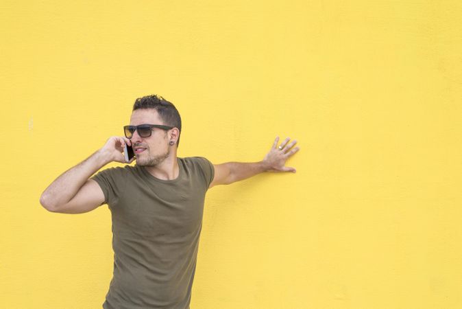 Serious male leaning on yellow wall talking on smartphone