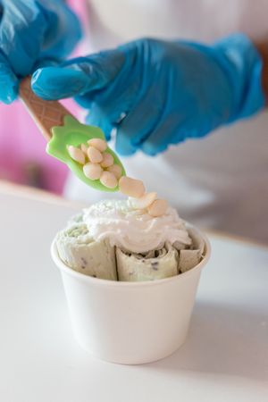 A worker is decorating a rolled ice cream tub with yogurt bubble toppings with a spoon