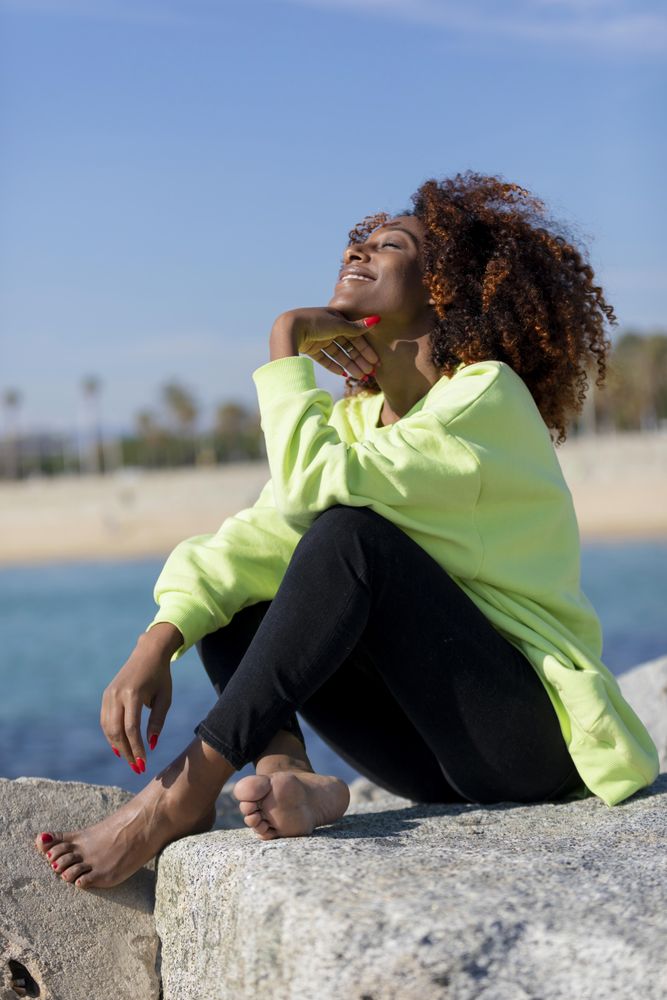 Happy female in green shirt sitting on rocks near coast