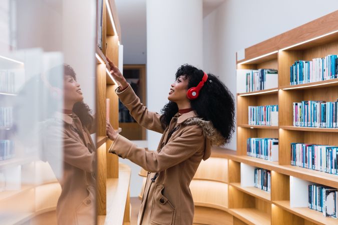 Satisfied woman with headphones taking book in library