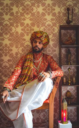 Man wearing turban and traditional Indian outfit sitting on chair indoor