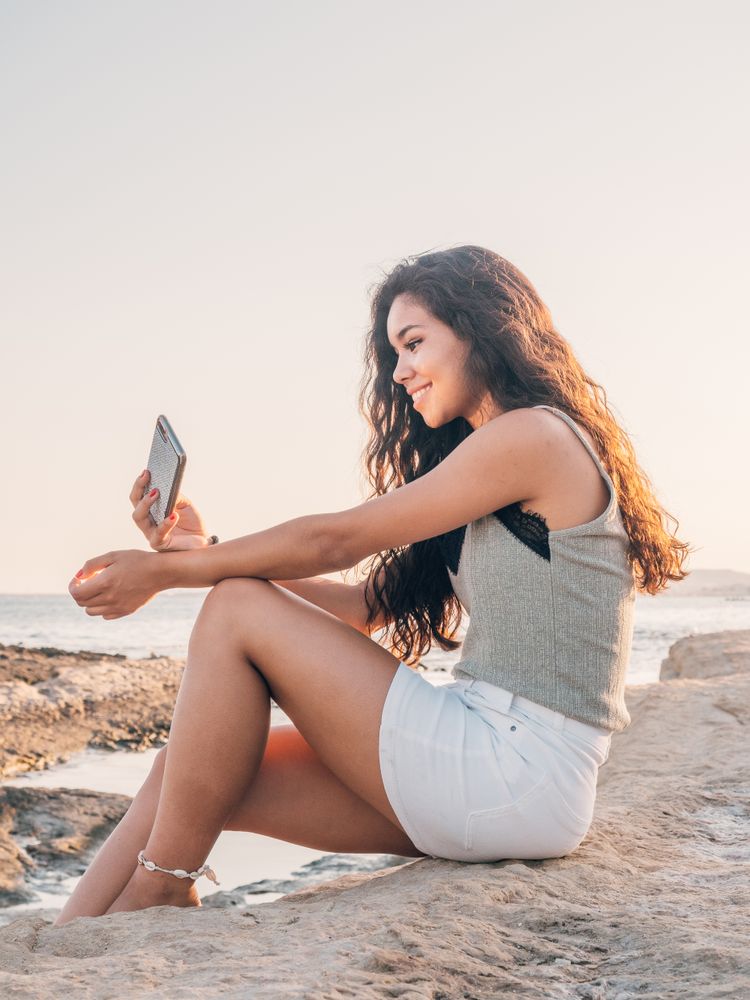 Dreamy trendy young woman texting on beach