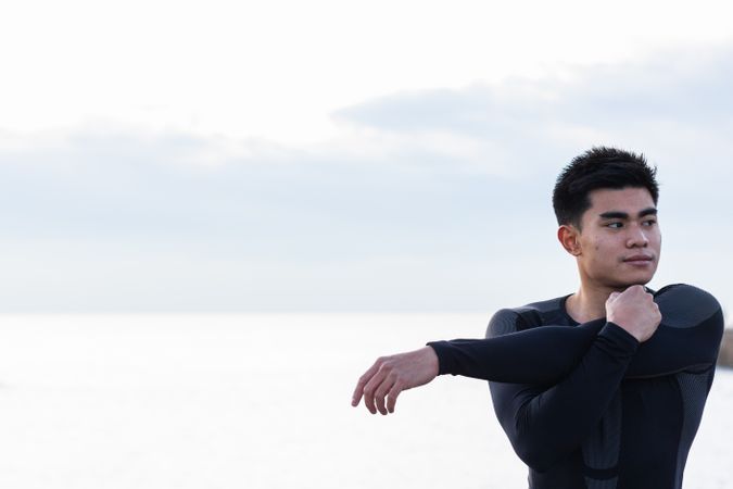 Asian sportsman stretching shoulders near sea