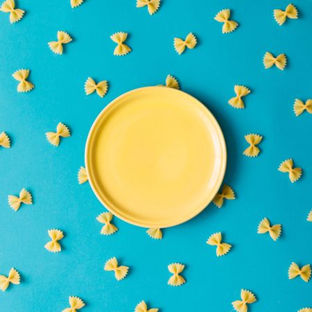 Pattern made of pasta on blue background with yellow bowl