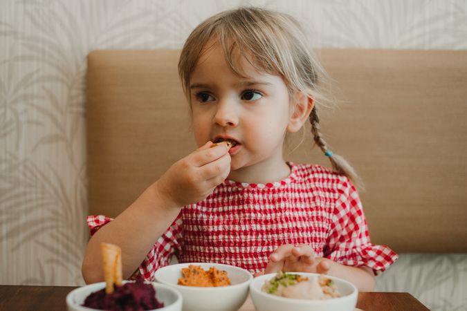 Girl eating with hand assorted food at table