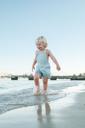 Innocent positive cute toddler strolling in waves of sea on coas