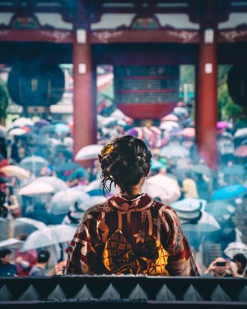 Back view of a woman in kimono with crowd of people holding umbrella on street as a background