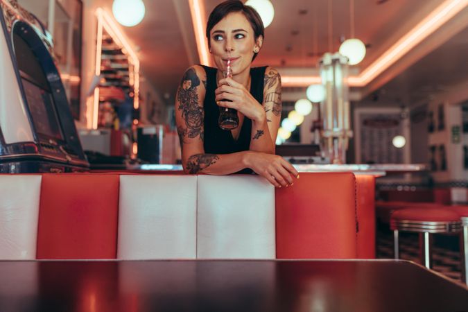 Happy woman standing in a cafe drinking a soft drink looking away