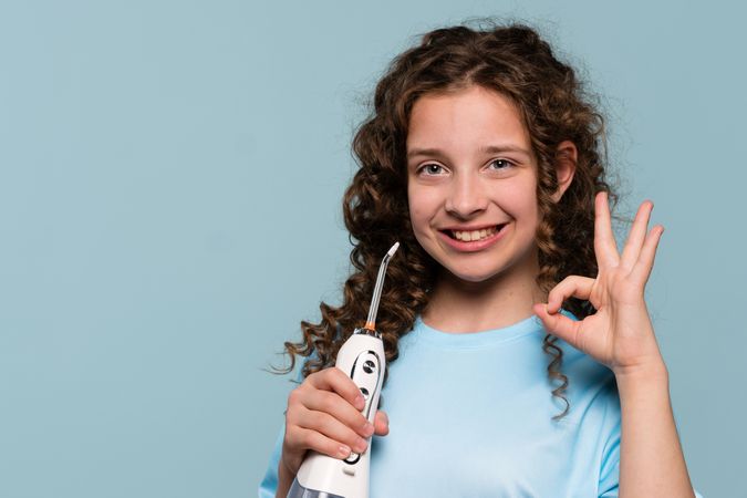 Girl giving OK sign, holding oral irrigator.