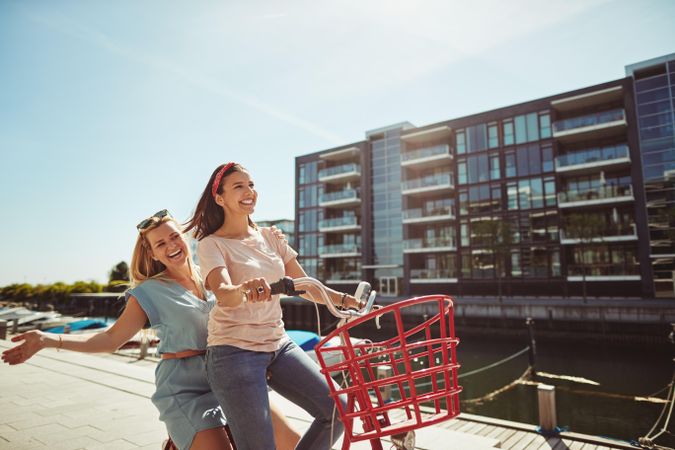 Two happy women riding a bicycle along the river walk