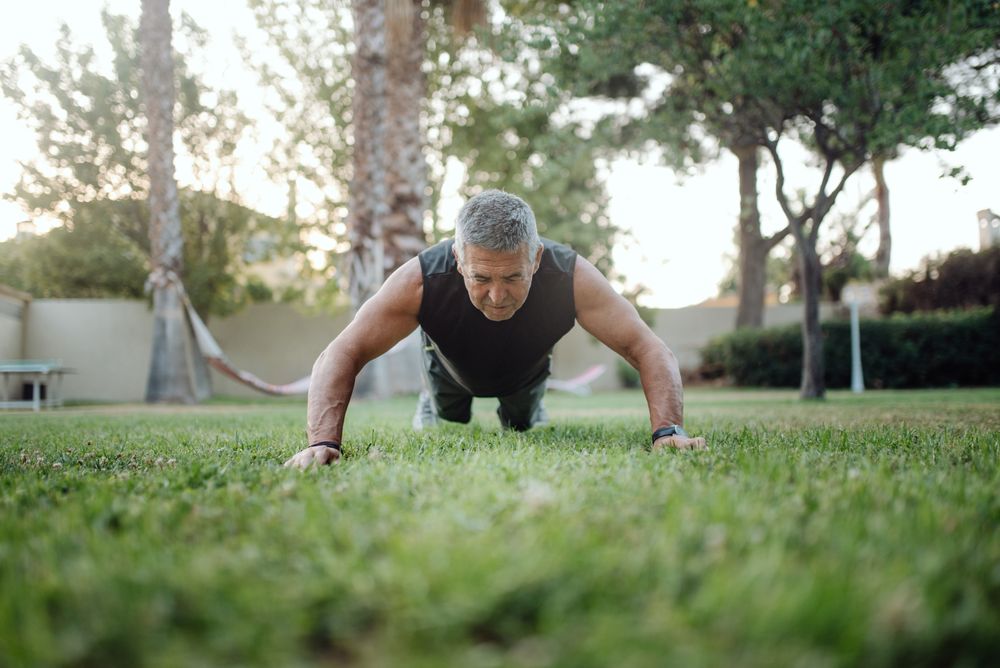Cheerful older man pushing ups on green grass in park