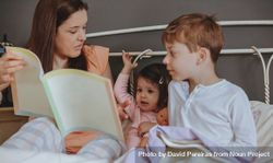 Portrait of mother reading book to her daughter and son in bed 4BApW5