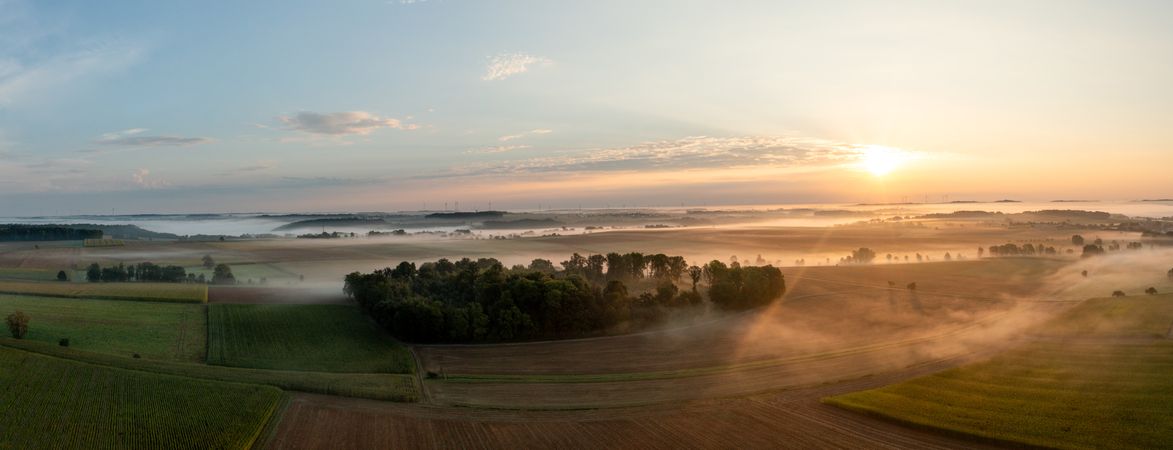 Drone scenery at golden hour with agricultural fields and rolling hills enlightened by sunrise