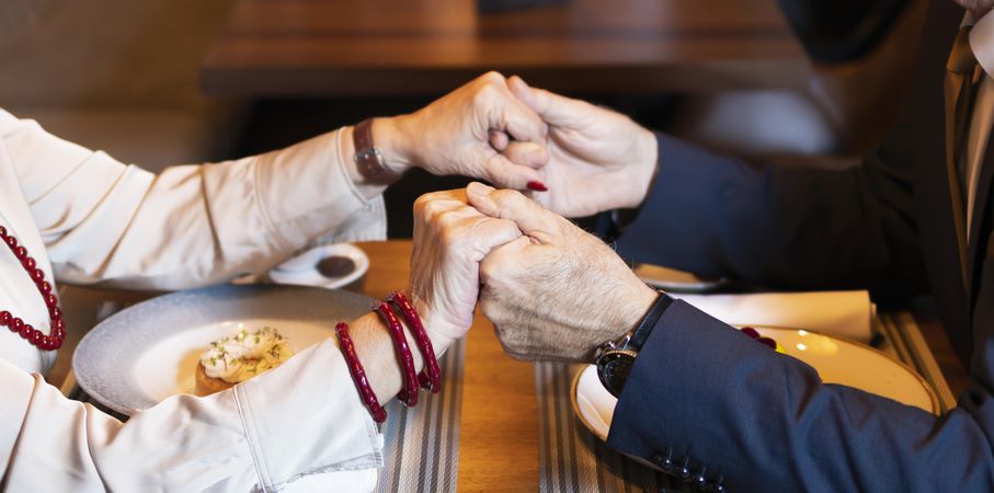 Close up of older couple holding hands over restaurant table