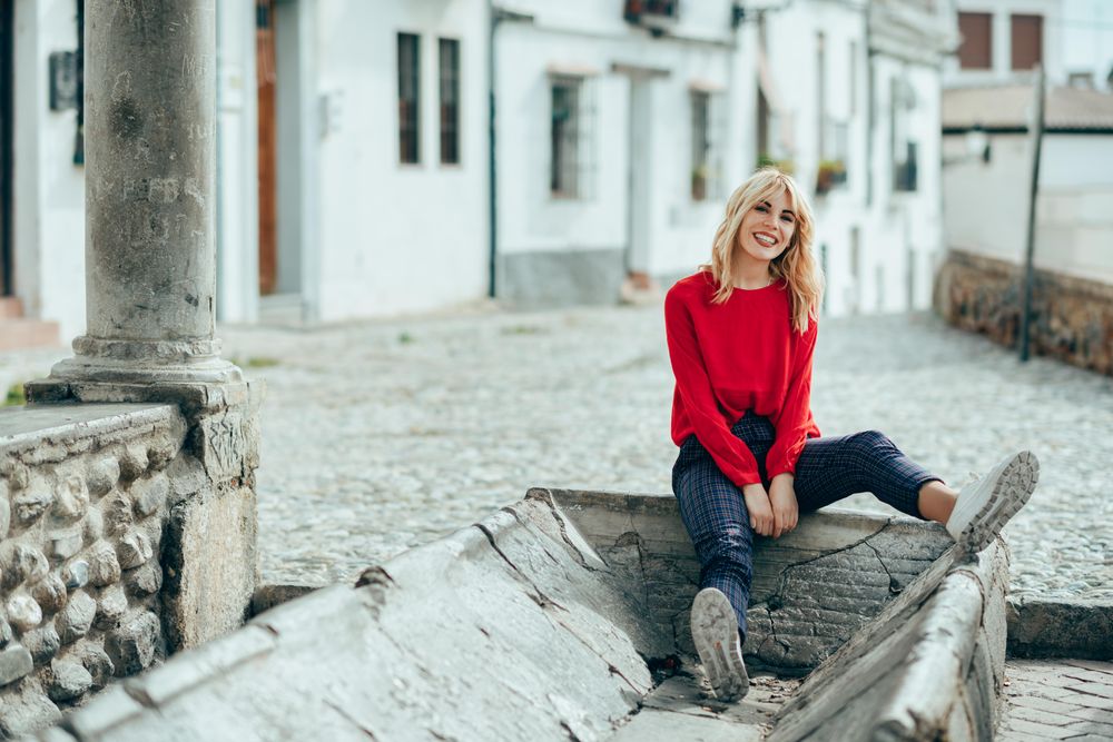 Happy young blond woman sitting on cement trough in Spanish town