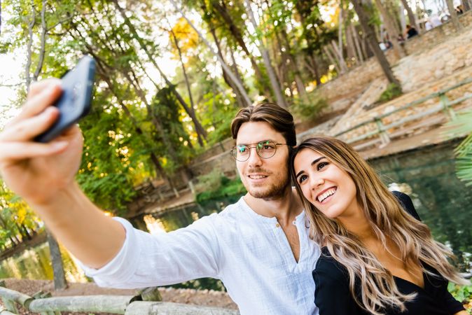 Smiling man and woman standing and taking photo near body of water
