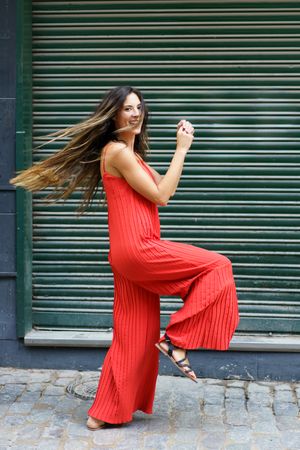 A woman in a bright red jumpsuit poses playfully outdoors, radiating joy and confidence
