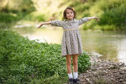 Girl in dress standing by river with her arms open