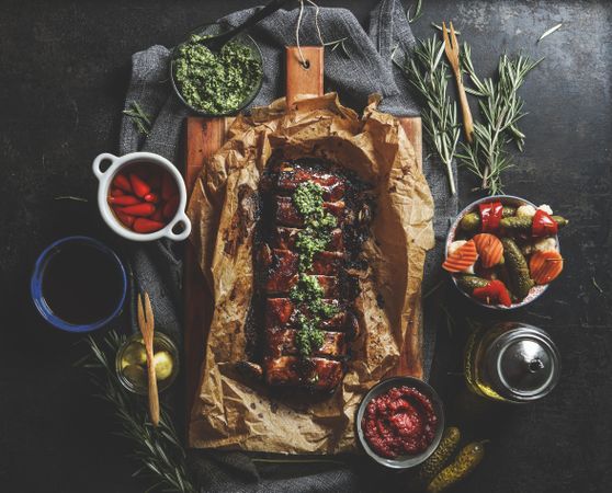 Roasted BBQ ribs with homemade pesto, pickled vegetables, sauces and rosemary on dark concrete kitchen table