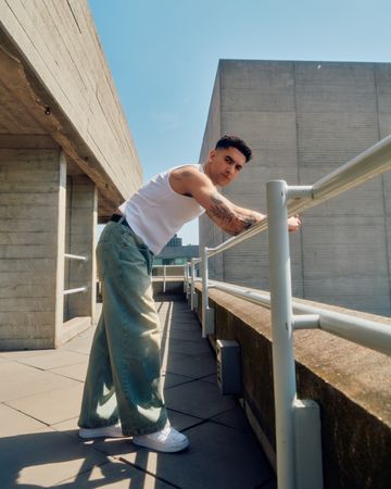Side of man in vest and jeans leaning on rail among concrete structures