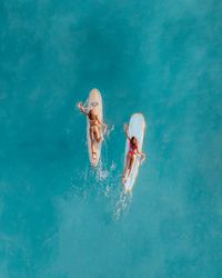 High-angle view of two women on a surfboard in water 0VJNv0