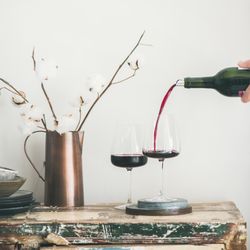 Wine glasses being poured from bottle with dried cotton in vase, square crop
