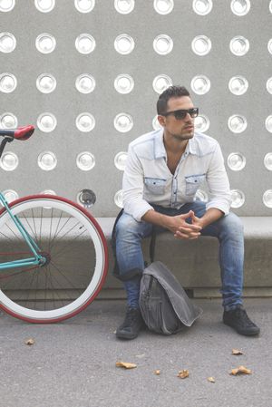 Male sitting with bike parked in front of patterned cement wall, vertical
