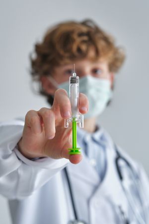 Boy doctor in sterile mask with plastic syringe