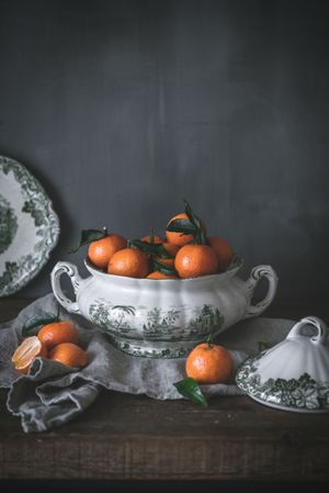 Orange tangerines in ceramic ornamental bowl on wooden table
