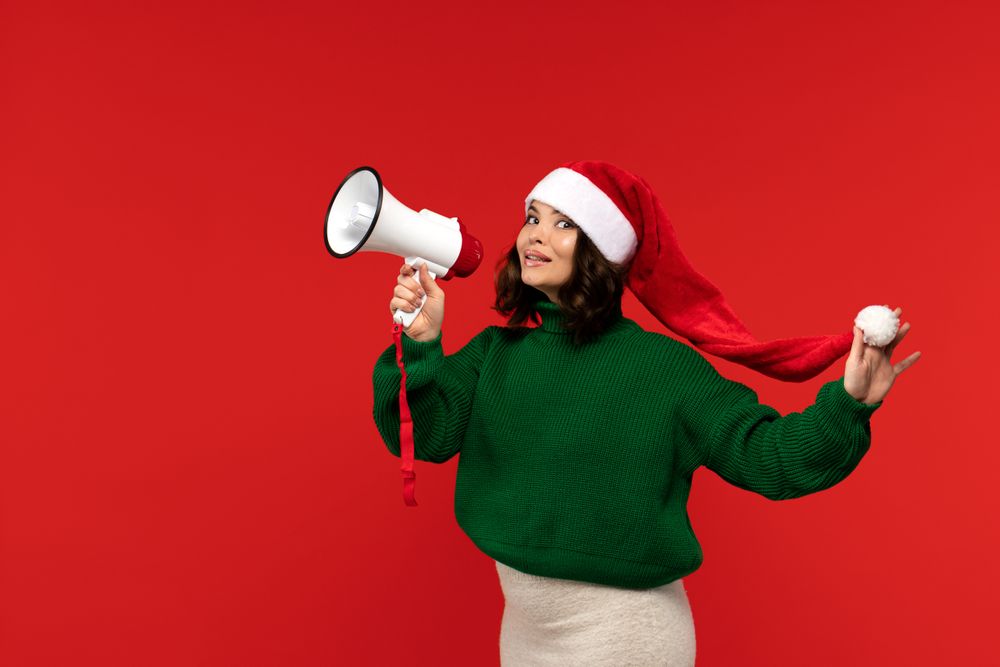 Smiling woman in Santa hat holding megaphone, playfully posing.