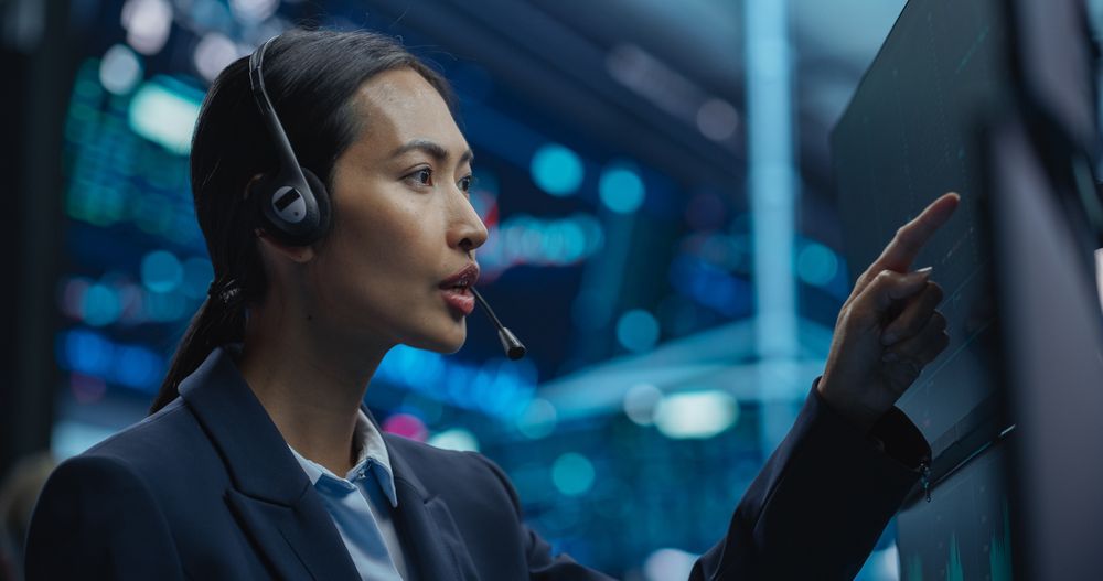 Asian Female Stock Exchange Broker Working on a Computer with Stock Information, Commodities and Exchange Market Charts