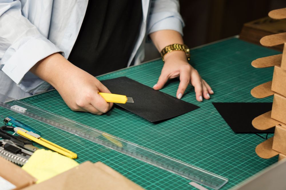 Hands of woman using sharp knife when cutting paper for making notebook