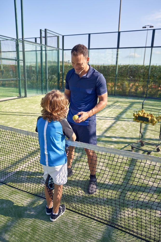 Coach with boy chatting during padel game on sports ground