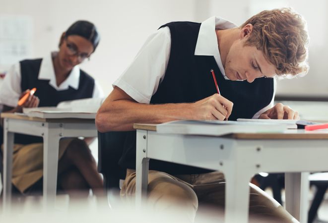 Teenage boy is taking a test while sitting at desk in classroom in high school