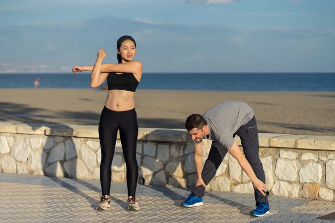 Young couple in active wear going stretching exercises together at seaside