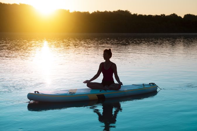 Rear view of woman peacefully meditating on paddleboard