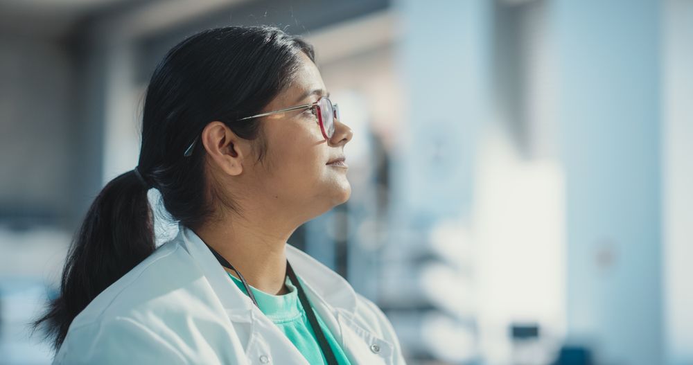 Profile Portrait Close Up of Young Indian Female Specialist Wearing Lab Coat and Glasses.