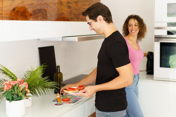 Couple smiling while assembling breakfast in bright kitchen