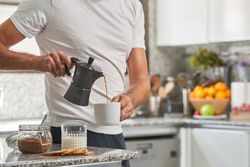 Crop man pouring coffee from moka pot in cup