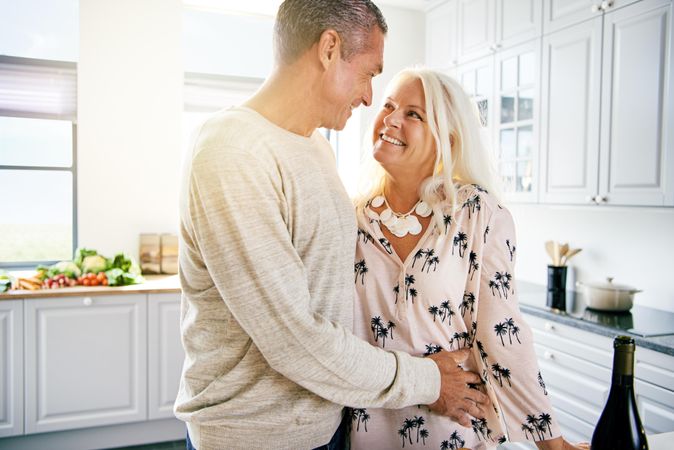 Mature couple embracing and looking at each other in bright kitchen