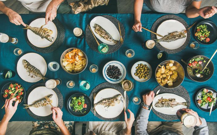 Group of people, and cat at table with whole fish on each plate and vegetable side dishes