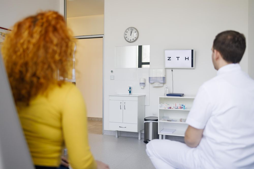Red haired female reading eye chart with optometrist