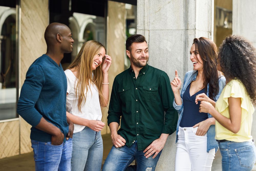 Group of women and men laughing together by city pillar