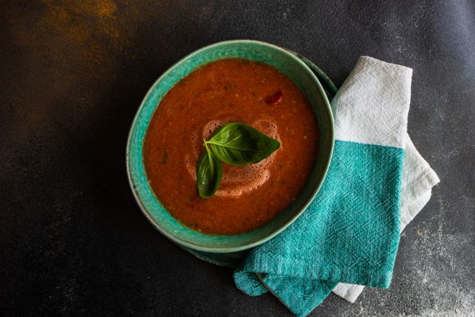 Green bowl of gazpacho soup with basil leaves on duotone napkin