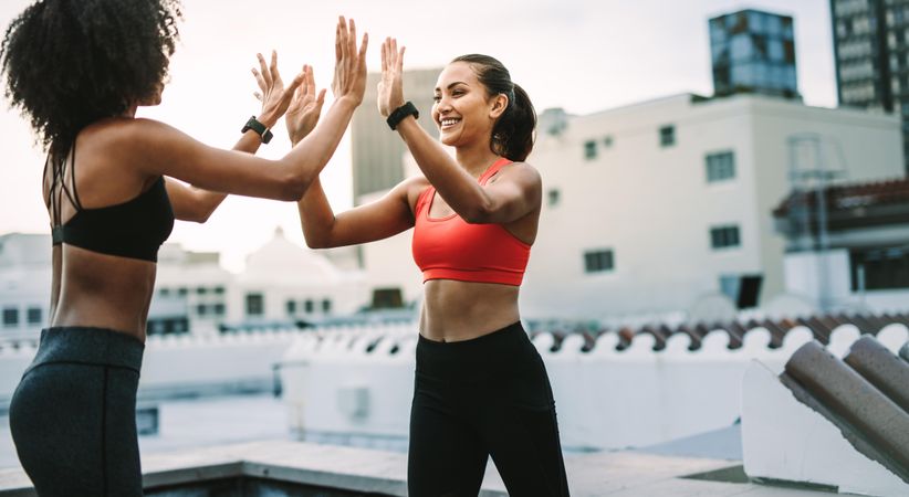 Two cheerful women in fitness wear giving high five during workout on the terrace