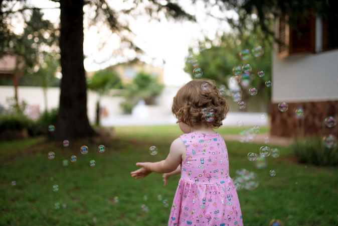 Joyful girl playing with colorful bubbles in grass