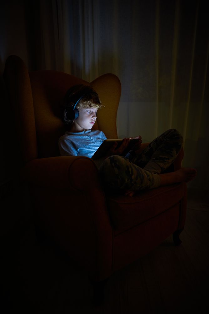 Boy in headphones playing on tablet in darkness