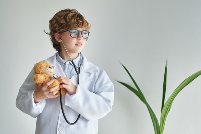 Dreamy boy in medical uniform examining toy bear with stethoscop