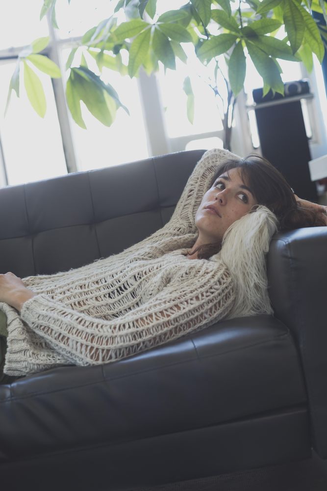 Female in wooly sweater relaxing on leather couch in living room, vertical